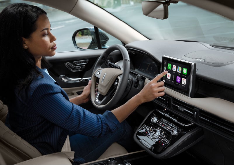A woman in the driver's seat of a 2022 Lincoln Corsair is touching the center digital screen to connect to Apple CarPlay® | Evergreen Lincoln in Issaquah WA