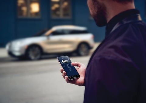 A person is shown interacting with a smartphone to connect to a Lincoln vehicle across the street. | Evergreen Lincoln in Issaquah WA
